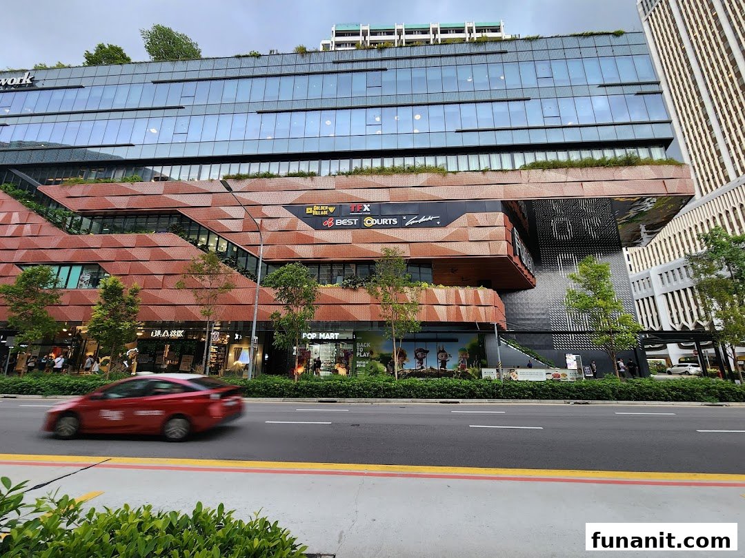 A modern shopping complex exterior with multi-level retail spaces, a street, and a red car passing by.