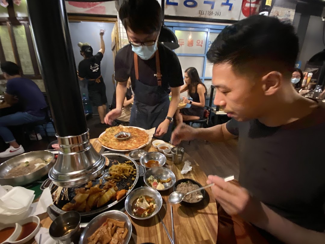 Diners enjoy a lively meal with a variety of dishes, including Korean BBQ and pancakes, served by staff.