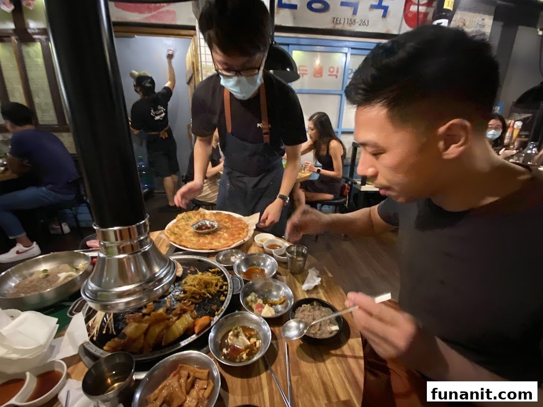 Diners enjoy a lively meal with a variety of dishes, including Korean BBQ and pancakes, served by staff.