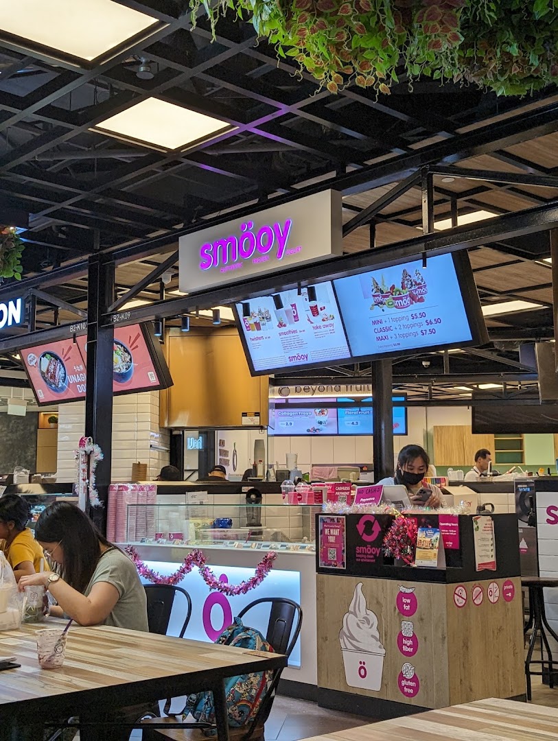 Interior view of smöoy frozen yogurt shop with customers and digital menu screens.