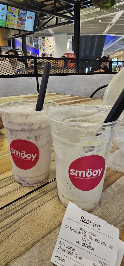 Two smöoy frozen yogurt drinks on a wooden table, one full and one nearly empty, with a receipt.
