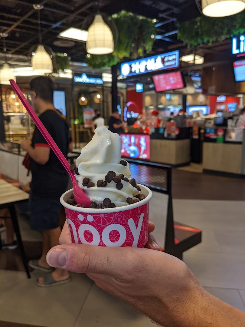 A hand holds a cup of smöoy frozen yogurt topped with chocolate chips and a pink spoon.