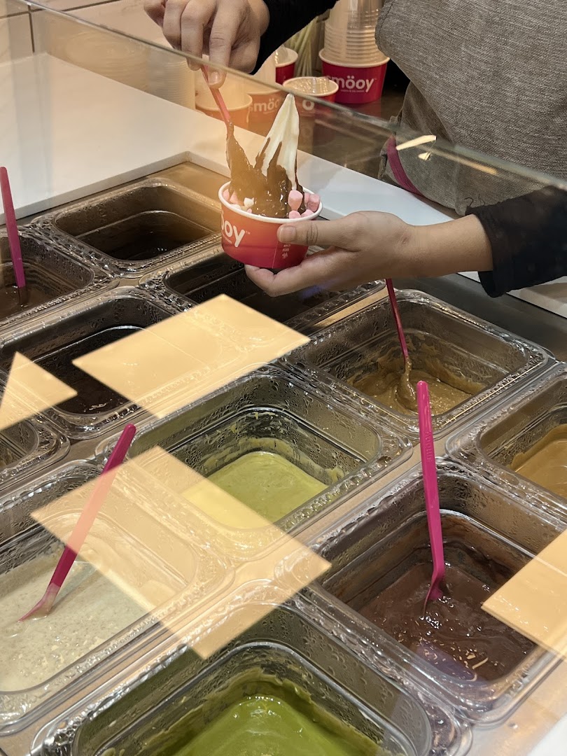 A person adds chocolate sauce to a frozen yogurt cup with toppings at smöoy.