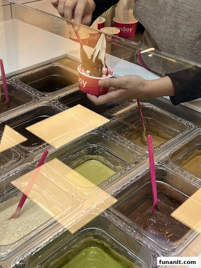 A person adds chocolate sauce to a frozen yogurt cup with toppings at smöoy.