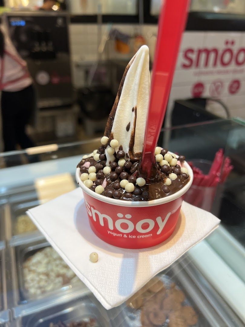 A delicious smöoy frozen yogurt with chocolate sauce and crunchy toppings in a red cup.