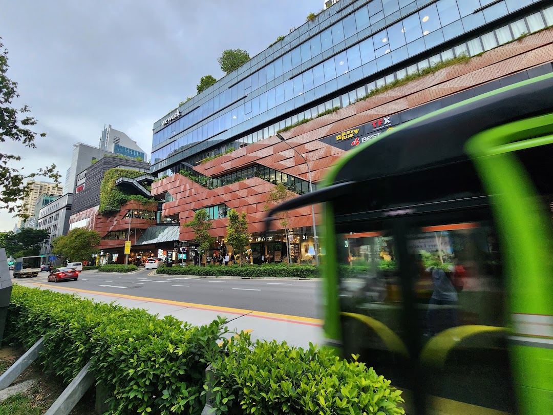 Exterior view of a modern multi-story retail and office complex with lush greenery and a busy street.