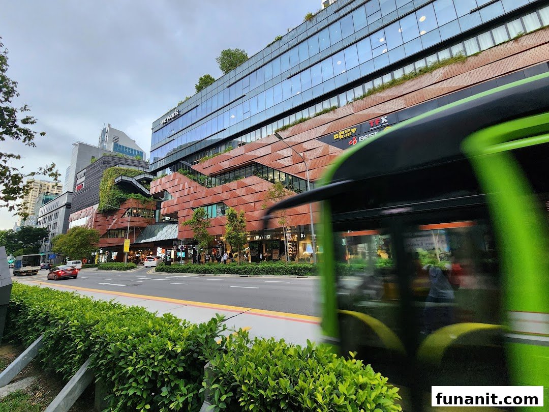 Exterior view of a modern multi-story retail and office complex with lush greenery and a busy street.