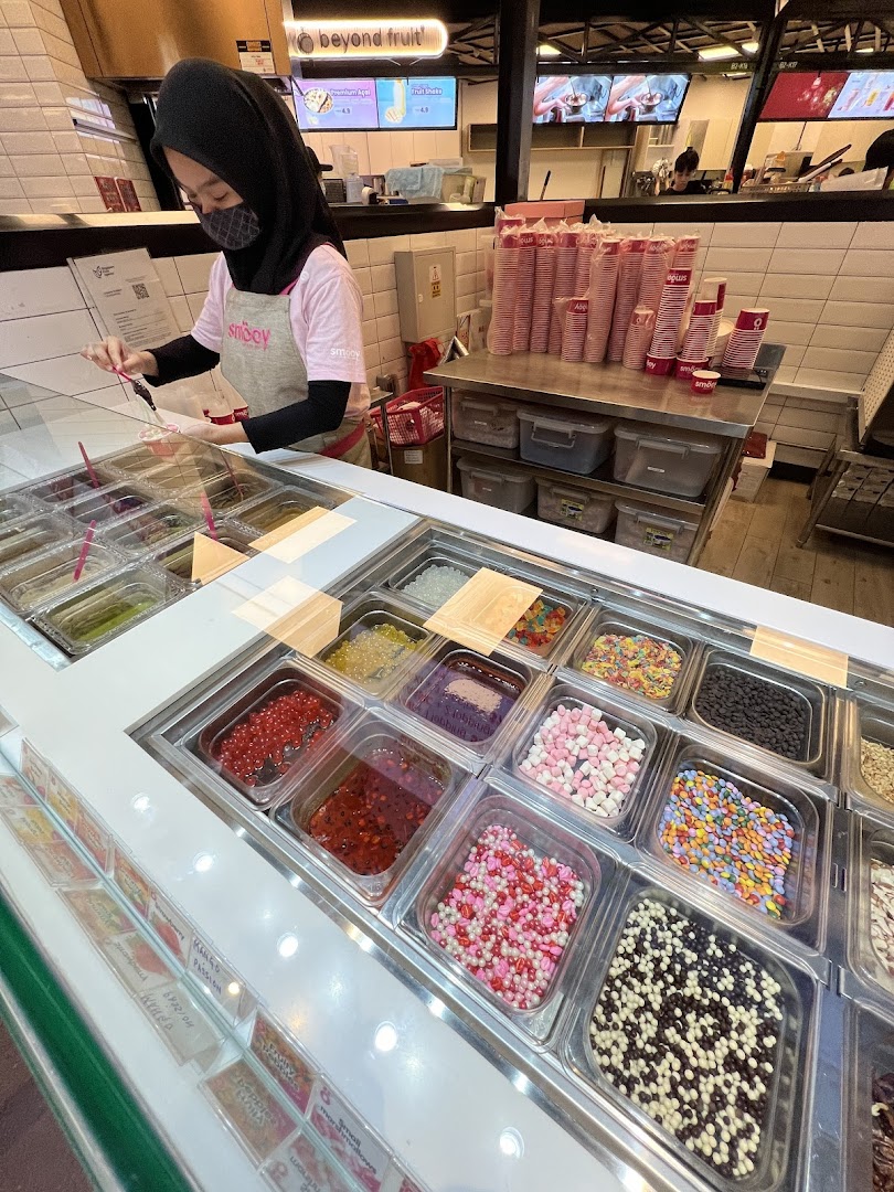 A smöoy staff member prepares a dessert with a vibrant array of toppings in a clean, modern shop.