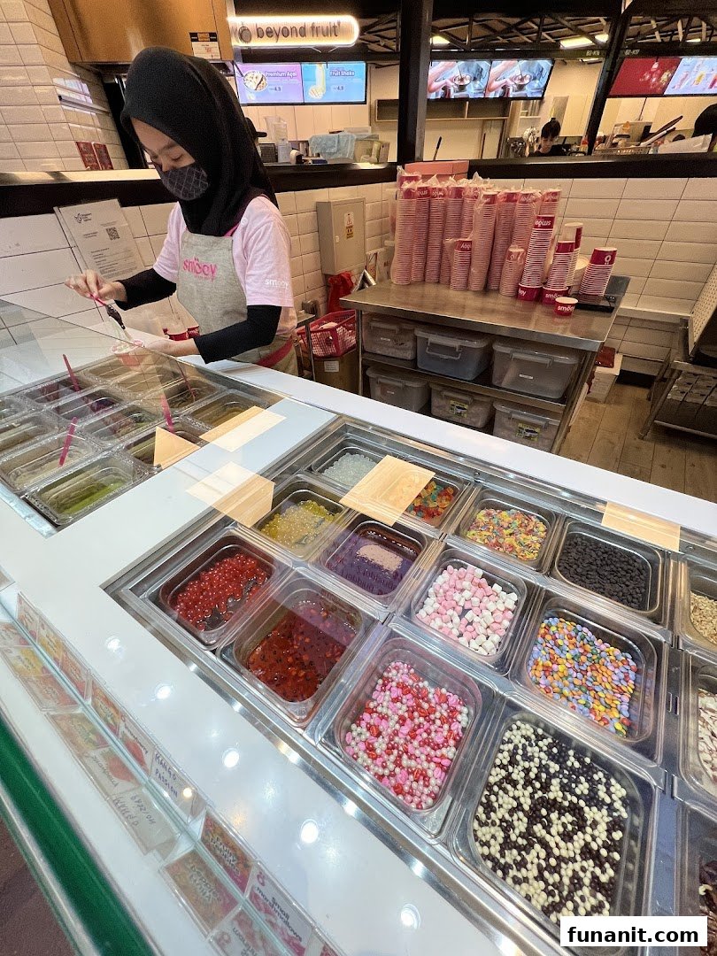 A smöoy staff member prepares a dessert with a vibrant array of toppings in a clean, modern shop.