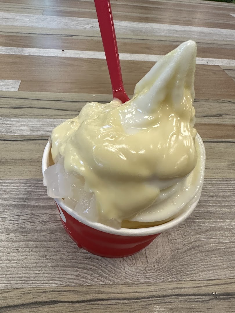 A close-up of a smöoy frozen yogurt cup with creamy topping and fruit jelly, served with a red spoon.