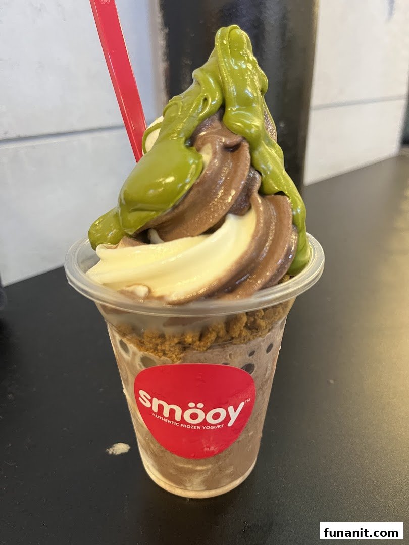 A close-up of a smöoy frozen yogurt cup with chocolate, vanilla, and green toppings.