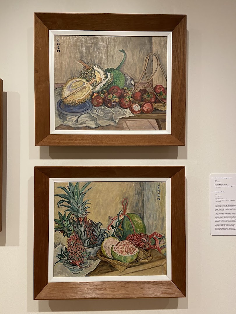 Two framed still-life paintings of tropical fruits displayed on a wall with an information plaque.