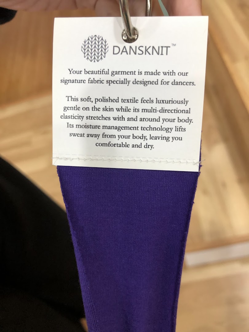 Close-up of a product tag detailing the features of DANSKNIT fabric on a purple garment.