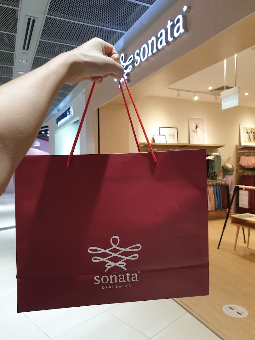A person holds a red Sonata Dancewear shopping bag in front of the store entrance.