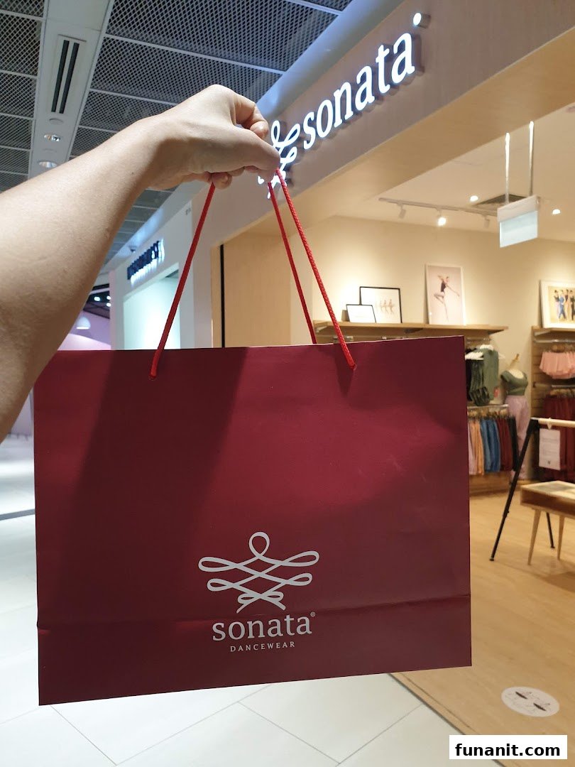 A person holds a red Sonata Dancewear shopping bag in front of the store entrance.