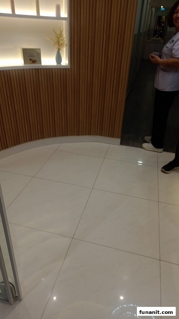 Modern interior with a curved wooden slatted wall, illuminated shelf, white tiled floor, and a staff member.