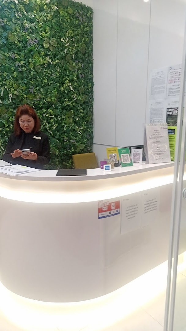 A staff member at a modern reception desk with a green wall, featuring payment QR codes and power bank rental.