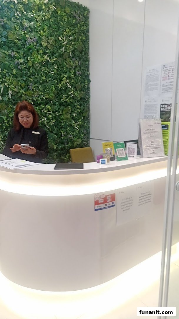 A staff member at a modern reception desk with a green wall, featuring payment QR codes and power bank rental.