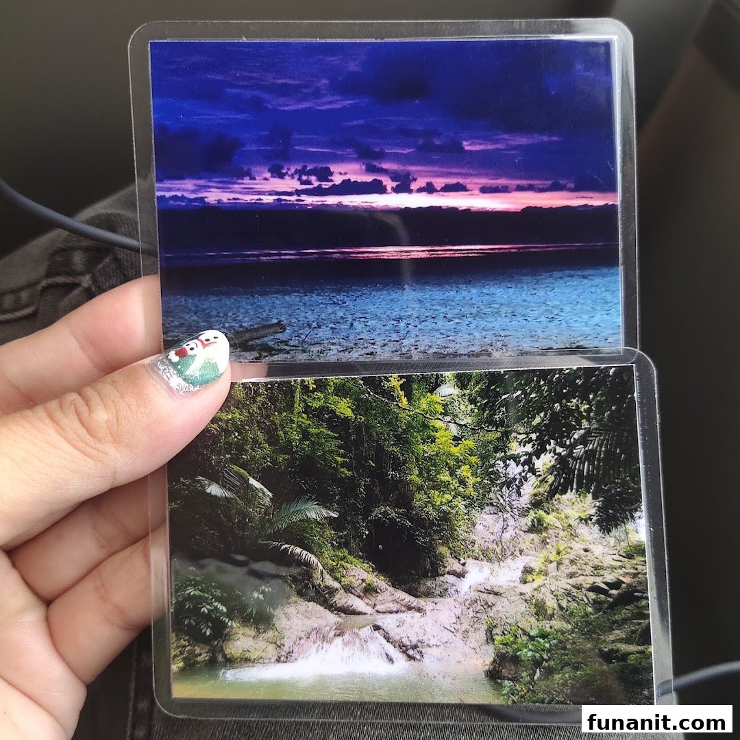 A hand holding two laminated photos: a vibrant sunset over water and a lush waterfall scene.