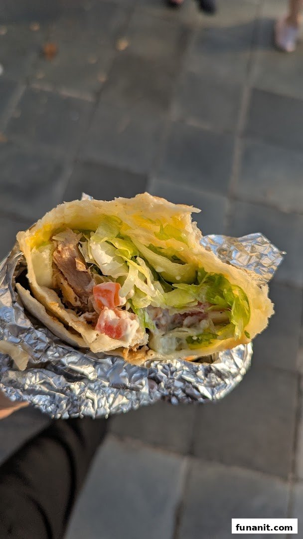 A close-up of a delicious, generously filled wrap with meat, fresh lettuce, and sauce, partially wrapped in foil.