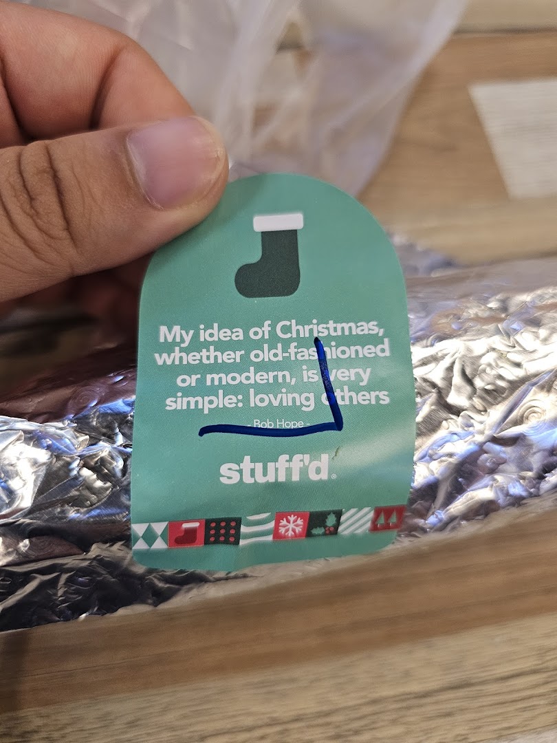 Hand holding a Stuffd brand tag with a Christmas quote and festive design.