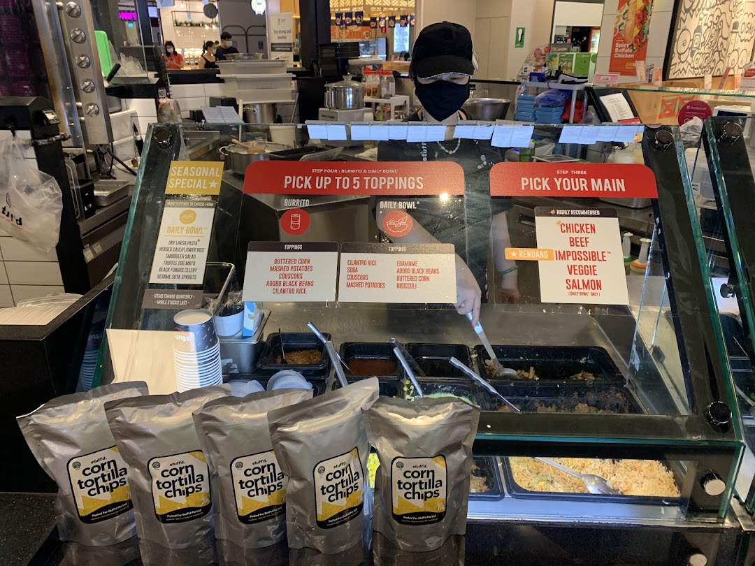 A Stuffd counter showing customizable burrito and bowl options with fresh ingredients and a staff member.