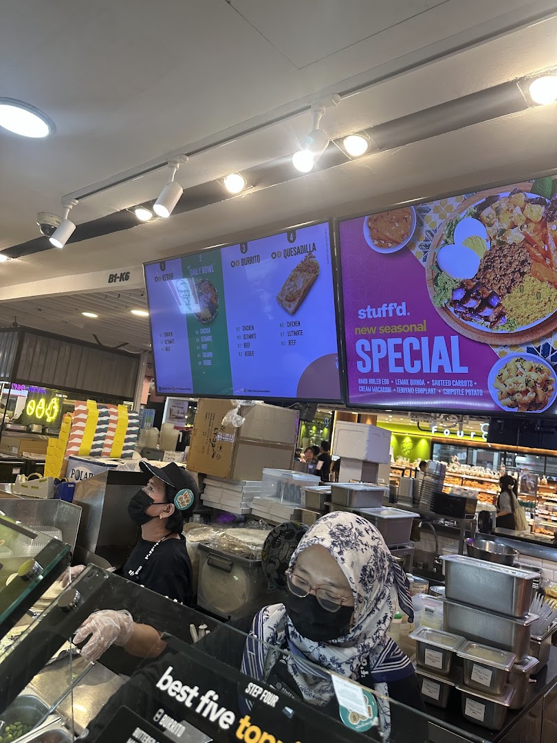Stuffd's vibrant counter with staff preparing fresh food, showcasing digital menus and seasonal specials.