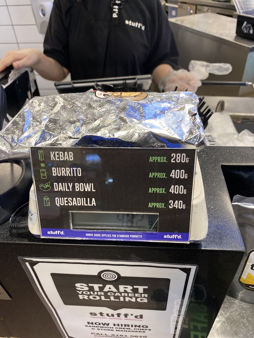 A counter display at Stuffd showing approximate weights for Kebab, Burrito, Daily Bowl, and Quesadilla.