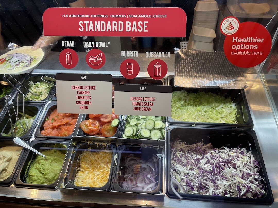 A vibrant food counter showcasing fresh ingredients and customizable meal options like kebabs, bowls, burritos, and quesadillas.
