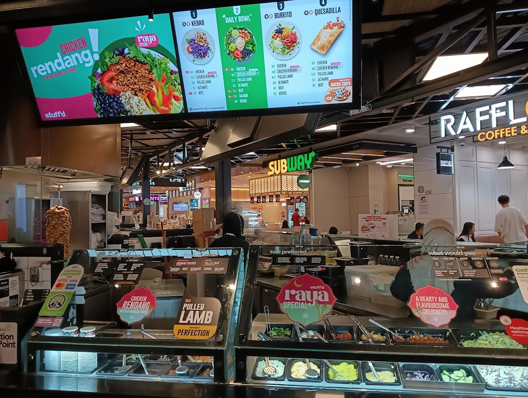 A vibrant food stall interior featuring a digital menu board displaying kebabs, bowls, burritos, and quesadillas.