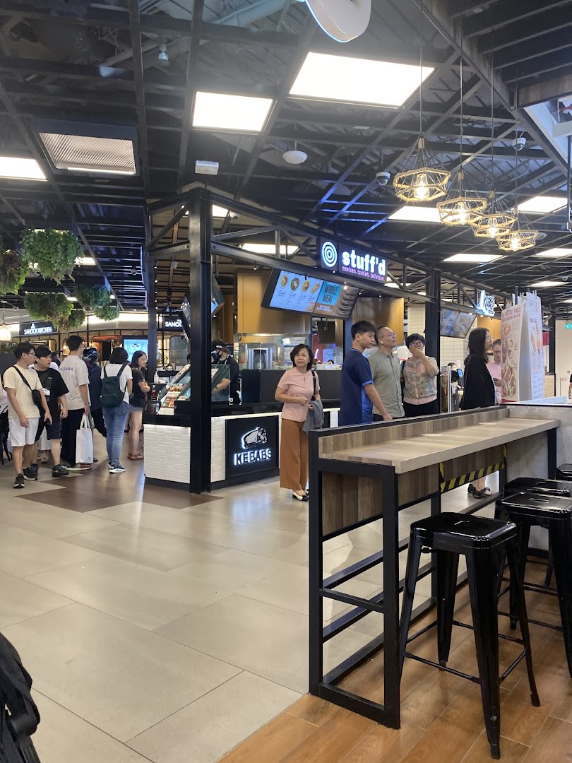 A bustling food stall named 'Stuffd' in a mall, with customers queuing and a nearby seating area.