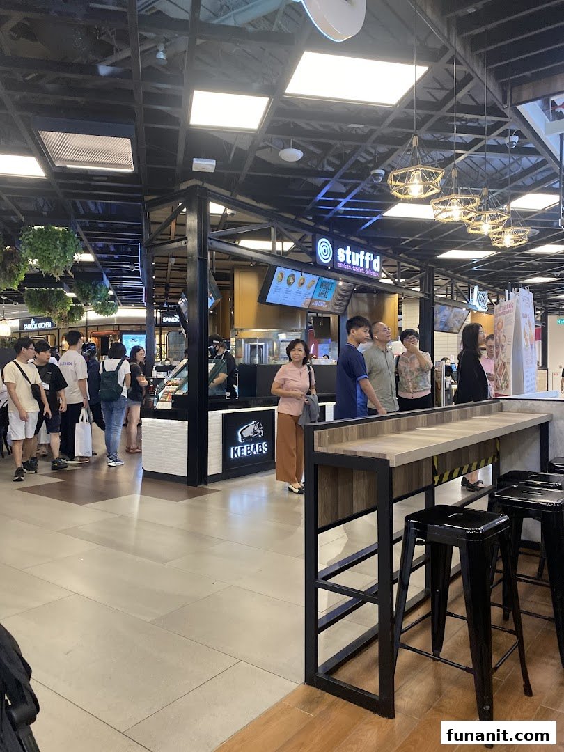 A bustling food stall named 'Stuffd' in a mall, with customers queuing and a nearby seating area.