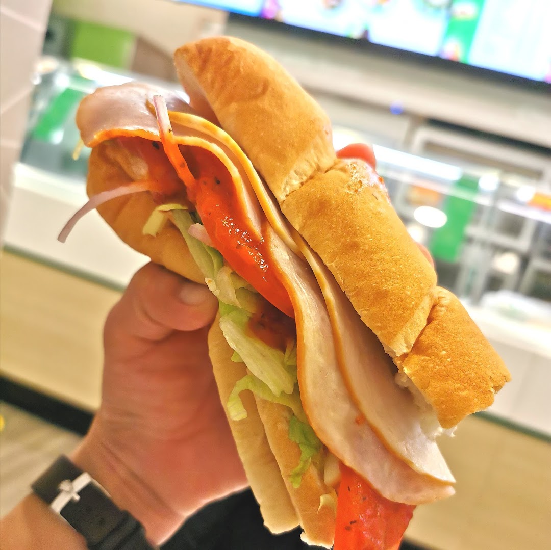 A hand holds a fresh Subway sandwich filled with turkey, lettuce, onions, and sauce.