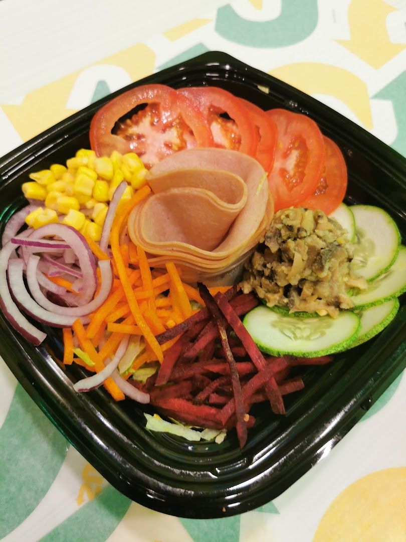 A vibrant Subway salad in a black bowl, featuring fresh vegetables and cold cuts.