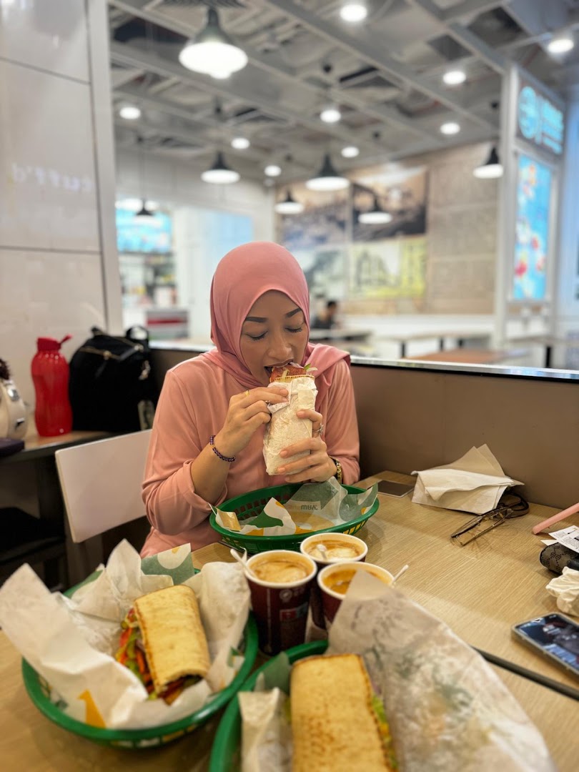 A person enjoys a fresh Subway sandwich at a table with other subs and drinks.