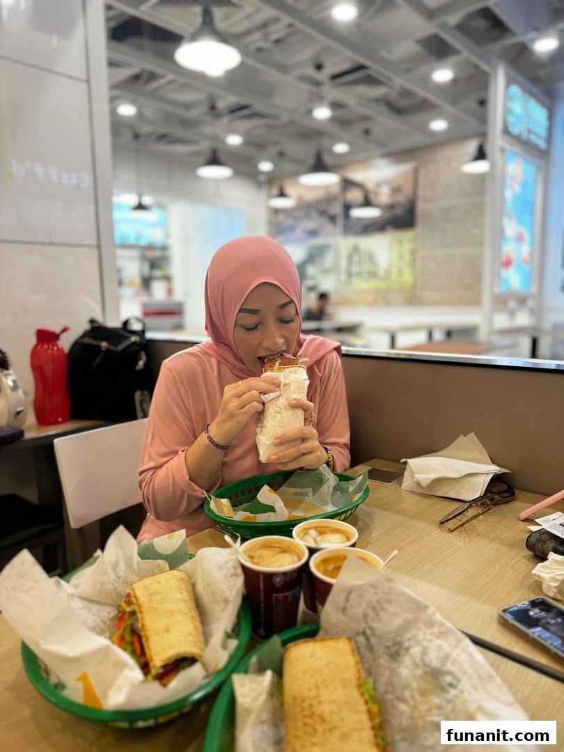 A person enjoys a fresh Subway sandwich at a table with other subs and drinks.