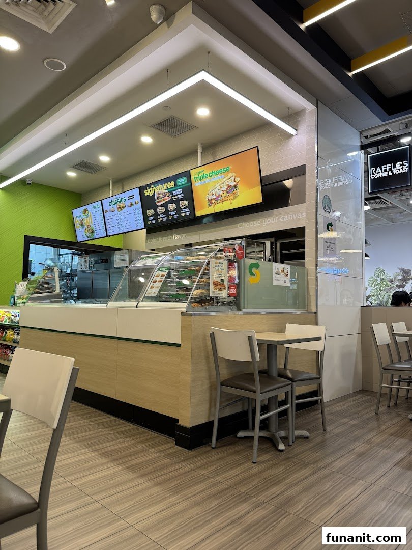 Interior view of a Subway restaurant featuring the counter, digital menu boards, and seating area.
