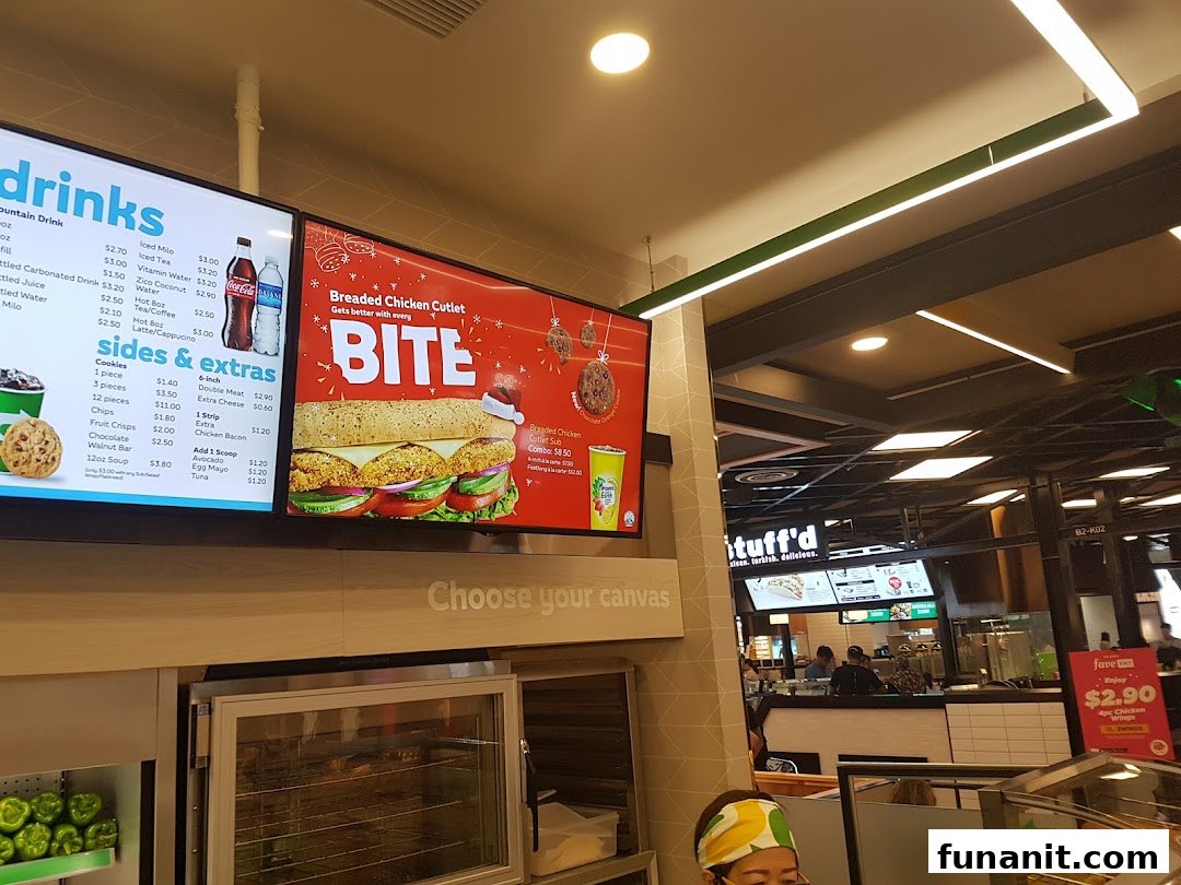 Interior view of Subway featuring digital menu boards, fresh ingredients, and counter area.