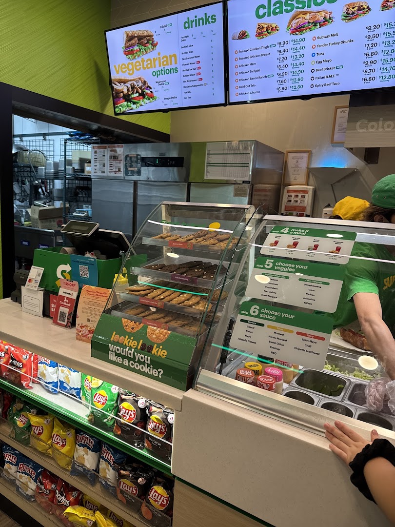 Interior view of a Subway restaurant, featuring the counter, digital menu boards, and snack displays.