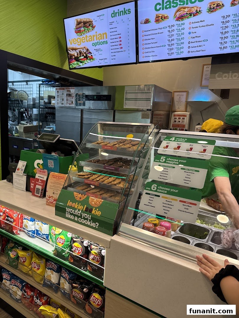 Interior view of a Subway restaurant, featuring the counter, digital menu boards, and snack displays.