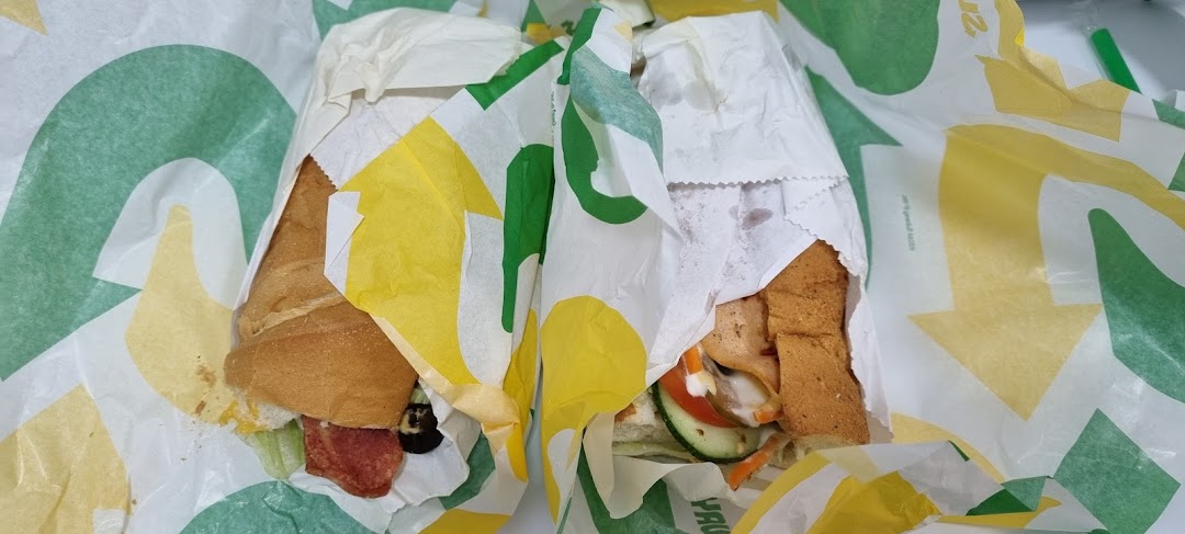 Two partially unwrapped Subway sandwiches, showcasing fresh ingredients and signature packaging.