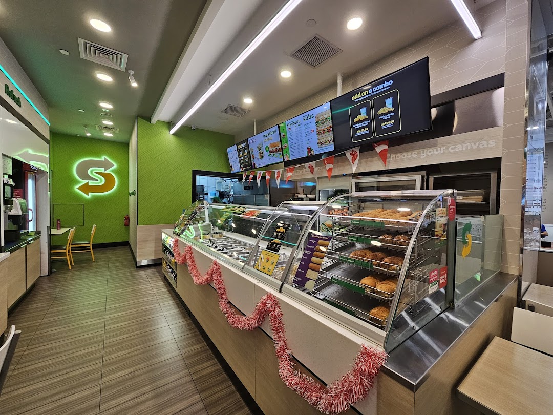 Interior view of a modern Subway restaurant with a service counter, digital menus, and seating.