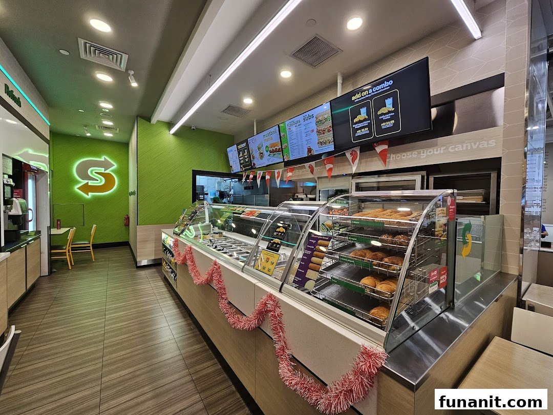 Interior view of a modern Subway restaurant with a service counter, digital menus, and seating.