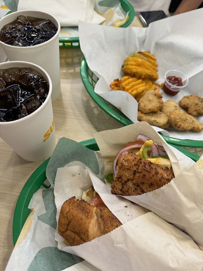 Two Subway sandwiches, waffle fries, chicken nuggets, and drinks on a table.