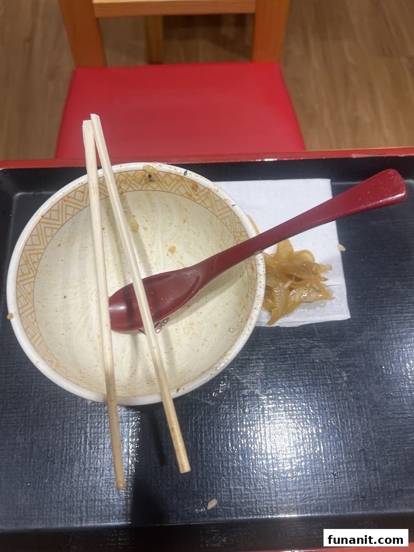 An empty bowl with chopsticks and spoon on a tray after a satisfying meal at Sukiya.