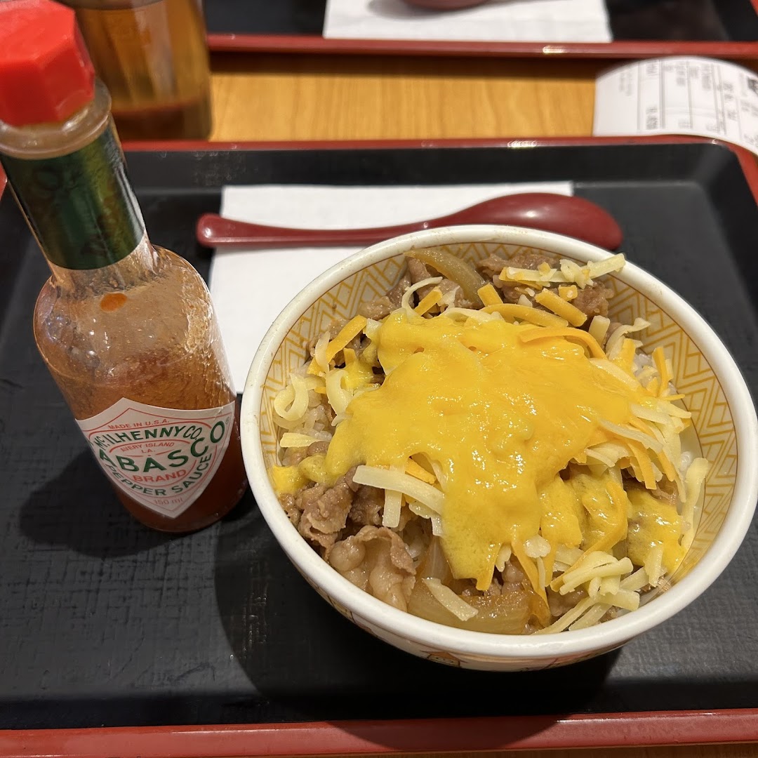 A close-up of Sukiya's gyudon bowl topped with melted and shredded cheese, served with Tabasco sauce.