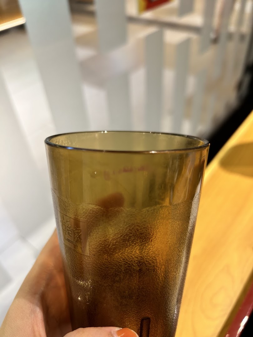 A close-up of a textured brown drinking glass held by a hand, with a blurry restaurant interior in the background.