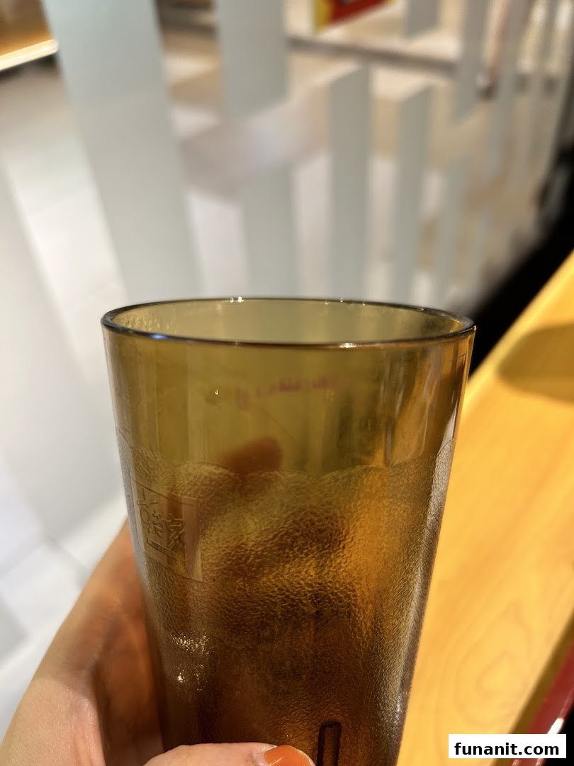 A close-up of a textured brown drinking glass held by a hand, with a blurry restaurant interior in the background.