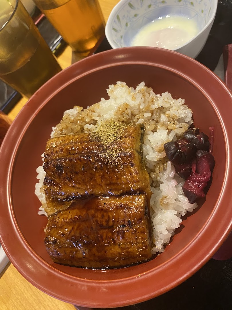 A close-up of a delicious unagi donburi with grilled eel, rice, and pickled vegetables.