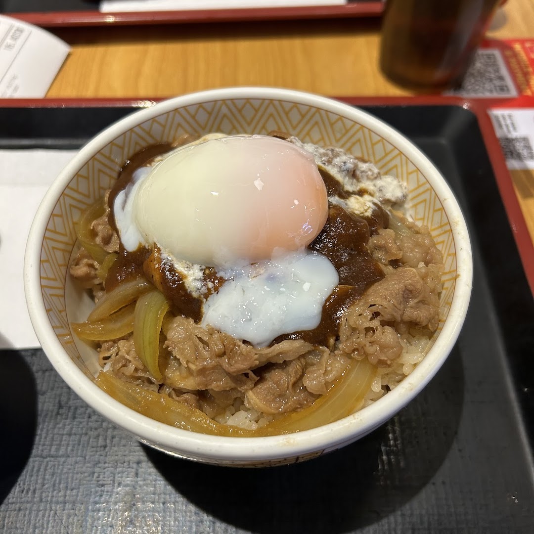 A close-up of a Sukiya Gyudon bowl with beef, onions, curry, and a soft-boiled egg.